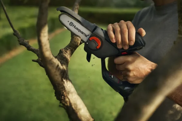 User using the Husqvarna Aspire P5-P4A cordless pruning saw to cut small branches in a garden setting.