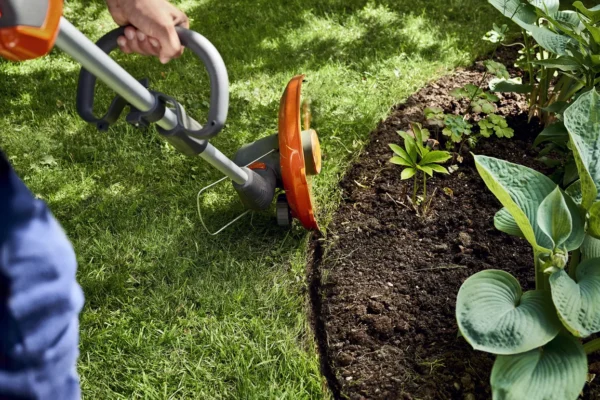 Person using Husqvarna 110iL FLXi cordless grass trimmer with loop handle to edge garden border.
