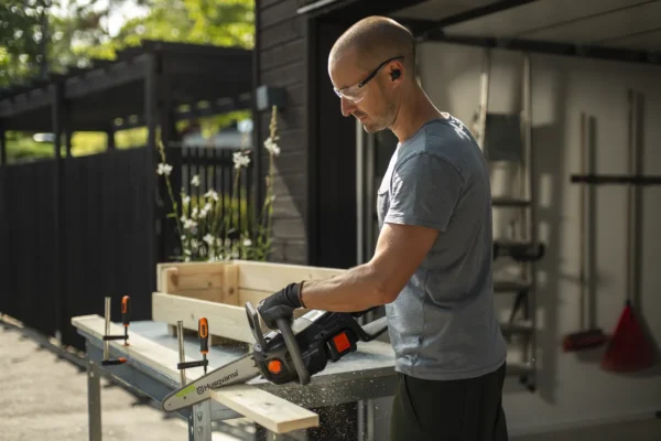 Man using the Husqvarna Aspire C15X-P4A5 cordless chainsaw to cut timber with precision during a DIY garden project.