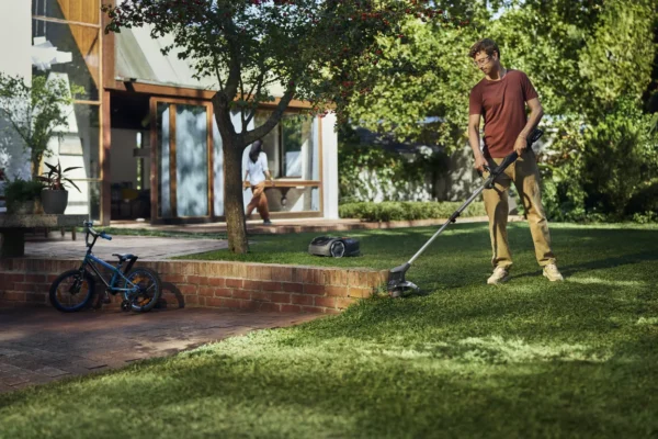 Man trimming lawn edge with Husqvarna Aspire T28-P4A cordless grass trimmer in modern garden