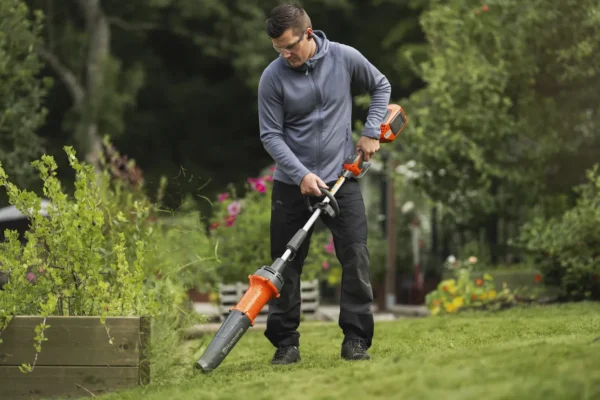 Man using the Husqvarna DB110 FLXi2 leaf blower attachment in a garden