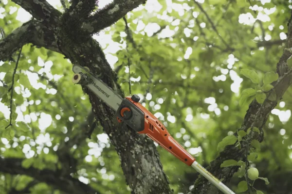 Husqvarna DP110 FLXi Pole Saw Attachment cutting a tree branch in a leafy outdoor environment.